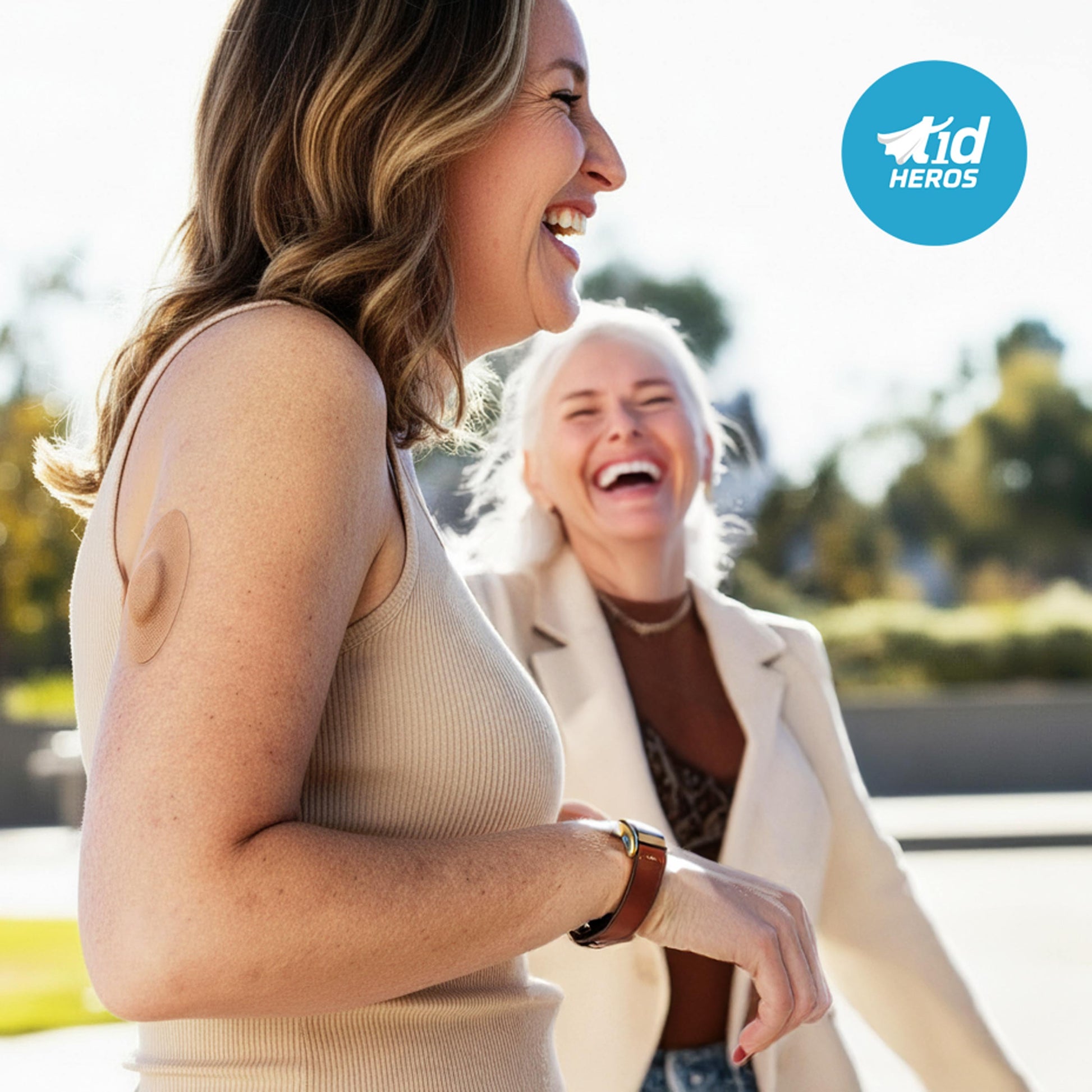 Two women laughing outdoors with a 'Tid Heros' logo in the corner.