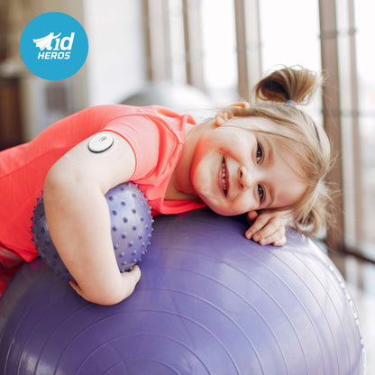 Child playing with a purple exercise ball indoors, with T1dHeroes logo in the corner.